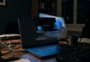 Laptop on a desk displaying Windows 11 setup screen, surrounded by cables and a mug in a dim office. Note: conveying the workspace and boot screen intent rather than just visuals.