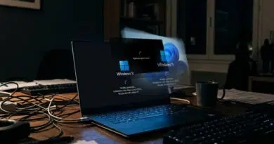 Laptop on a desk displaying Windows 11 setup screen, surrounded by cables and a mug in a dim office. Note: conveying the workspace and boot screen intent rather than just visuals.