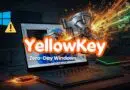 Laptop on a dark desk with fiery cyber effects and a vault exploding, overlaid with 'YellowKey Zero-Day Windows' text indicating a Windows exploit concept