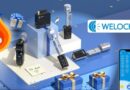 Promotional display of WELOCK smart locks and accessories on a blue platform with gift boxes and a large flame-shaped % off icon, suggesting a sale.