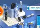 Promotional display of WELOCK smart locks and accessories on a blue platform with gift boxes and a large flame-shaped % off icon, suggesting a sale.