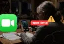 Person at a desk using a smartphone for video chat, with Zoom and FaceTime logos and a caution symbol in the foreground.
