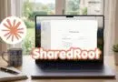 Laptop on a wooden desk displaying software UI with ShareDRoot branding; a mug, notebook, and small plant nearby.