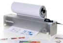 Openprinter desktop printer with a roll of paper feeding through, printing sheets in front of it