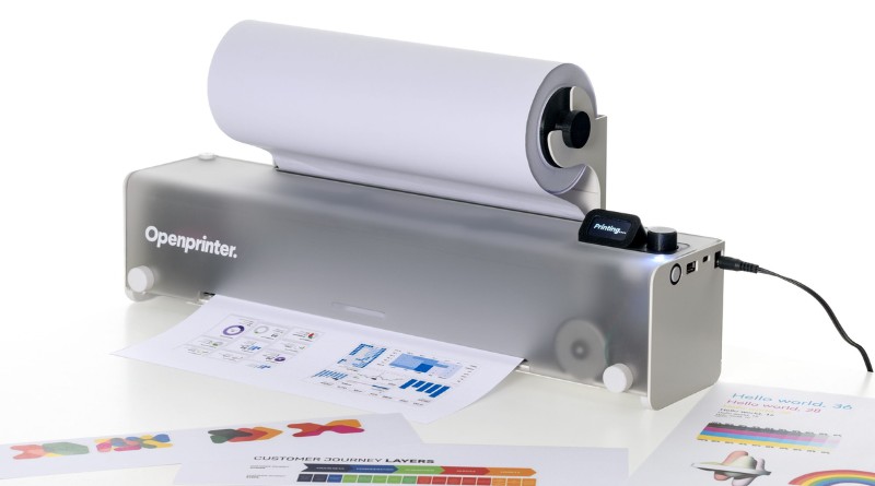 Openprinter desktop printer with a roll of paper feeding through, printing sheets in front of it