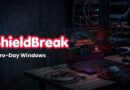 ShieldBreak banner over a hacker's dark workstation showing 'Zero-Day Windows' exploit text on a laptop screen in a data-center setting.